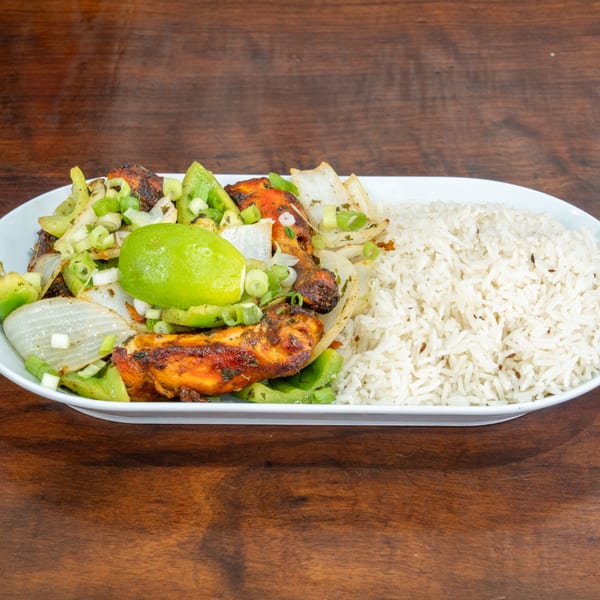 Grilled chicken with onions, peppers, and lime, served with white rice on a white plate.