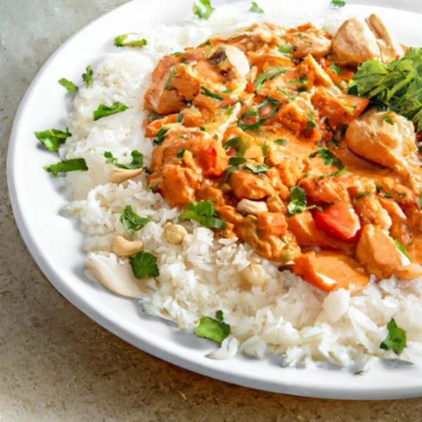 Spicee Bite's Indian butter chicken with rice, cashews, and fresh cilantro on a white plate.