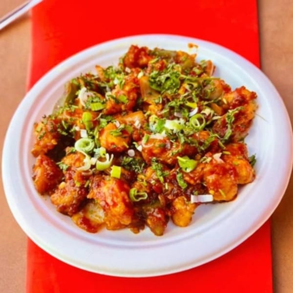 A white plate filled with Gobi Manchurian, garnished with green onions and cilantro.