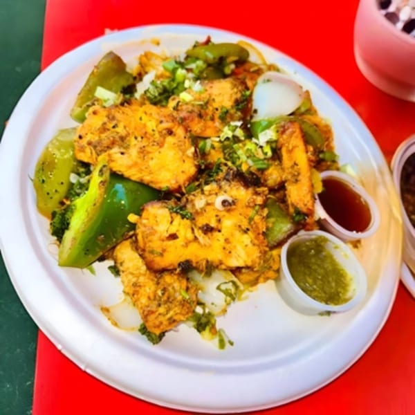 Indian paneer dish with green bell peppers, onions, and two dipping sauces on a white plate.