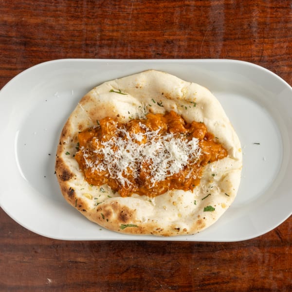 Naan bread topped with orange chicken curry and shredded white cheese on a white plate.