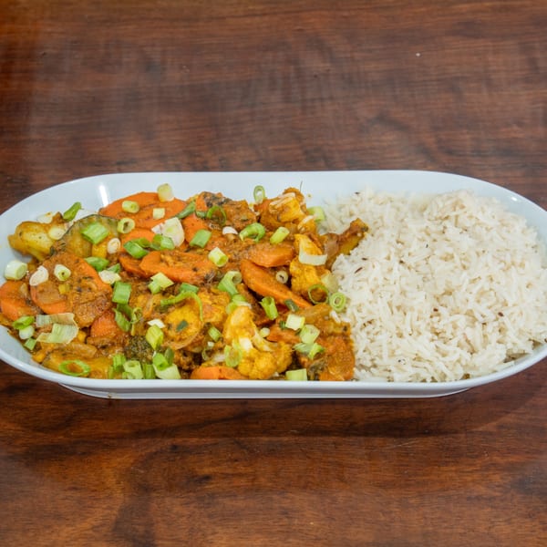 A white platter with vegetable curry and white rice, garnished with chopped green onions.