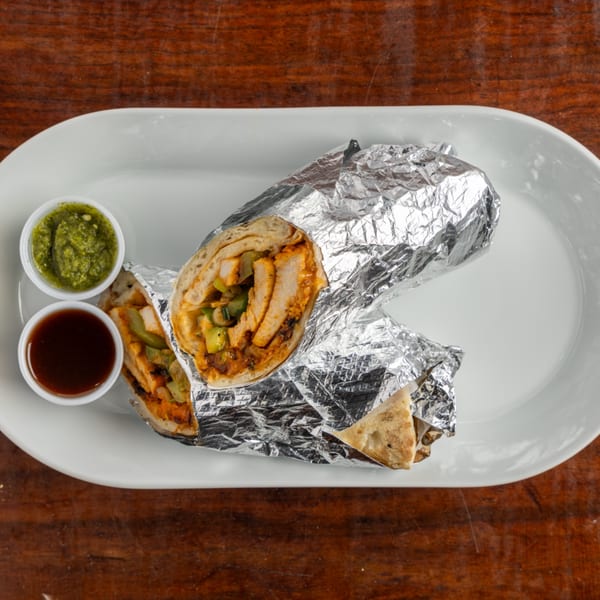 Two chicken wraps, partially unwrapped from foil, with green and brown dipping sauces on a white plate.