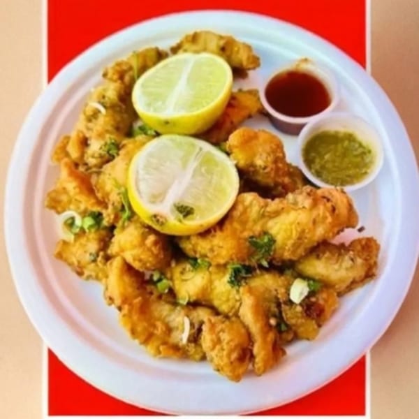 Crispy fried Indian pakora with lemon wedges, green chutney, and red sauce on a white plate.