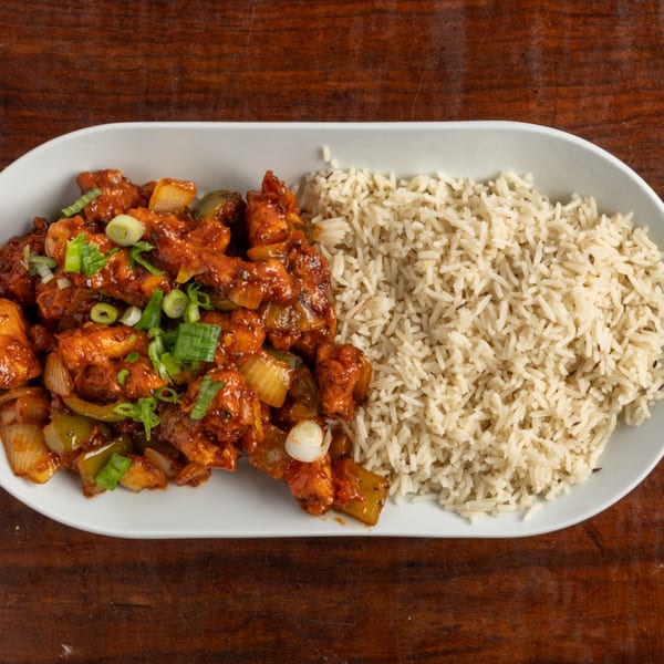 Spicy orange chicken with onions and green garnish, served with a side of white rice.
