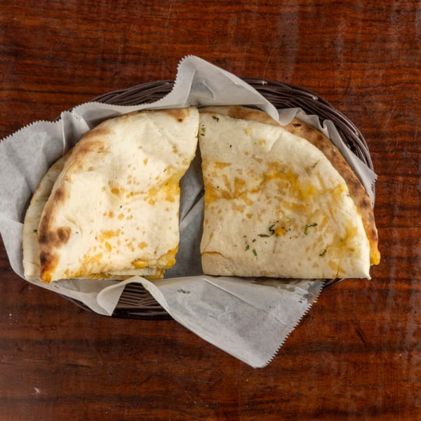 Two cheese quesadillas, cut in half, served in a basket lined with white paper on a wooden table.