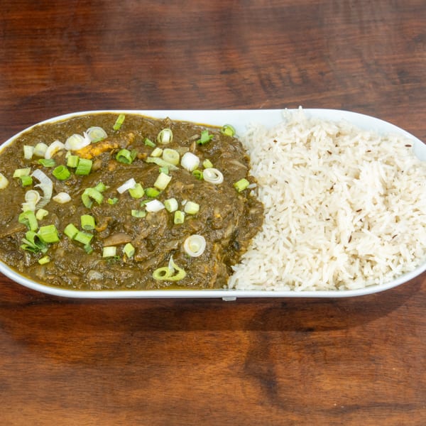 A white plate with green saag paneer topped with scallions, next to white rice.