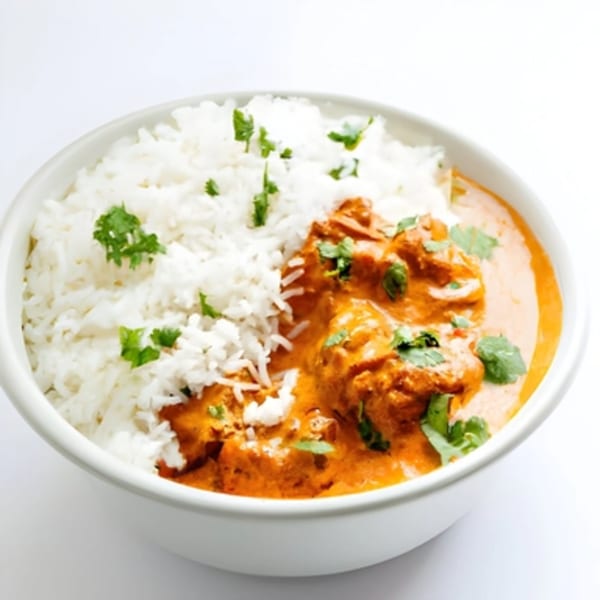 A white bowl filled with fluffy white rice and rich orange Indian butter chicken, garnished with fresh cilantro.