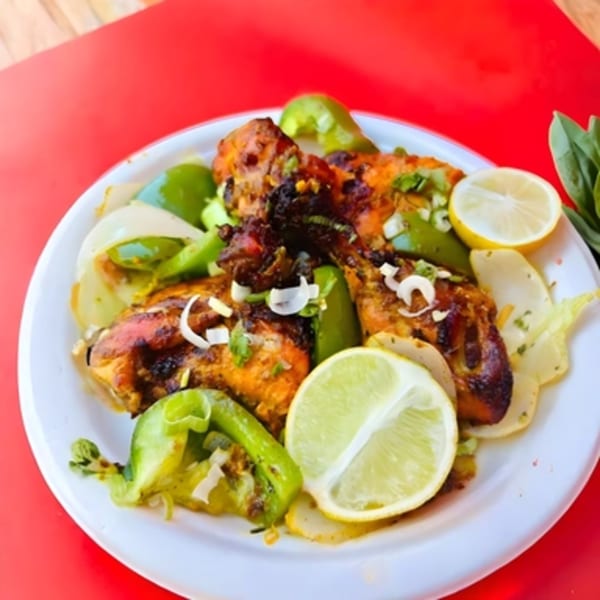 Spicee Bite's Indian chicken dish with green peppers, onions, and lemon slices on a white plate.