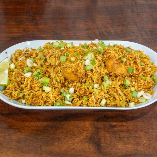A white oval platter filled with golden chicken biryani, garnished with chopped green onions and a lime wedge.