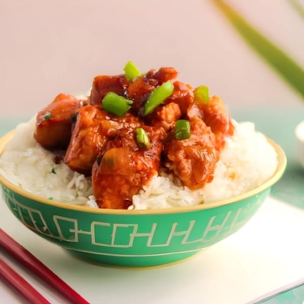 Indian chili chicken with white rice and green onions in a decorative green bowl.